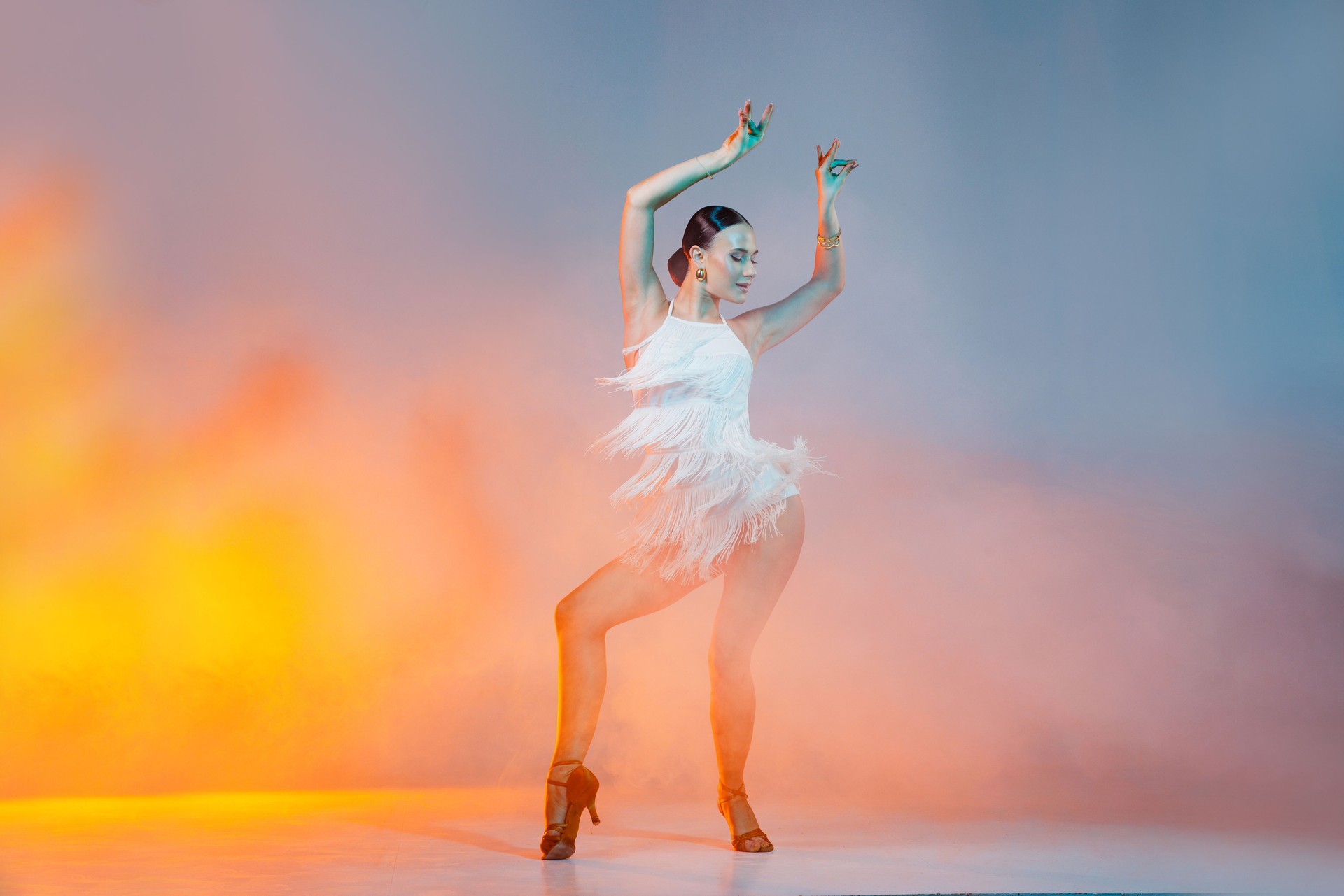 Passionate female dancer in a white fringe dress performing a dynamic Latin dance, surrounded by colorful stage smoke in an artistic and dramatic pose.